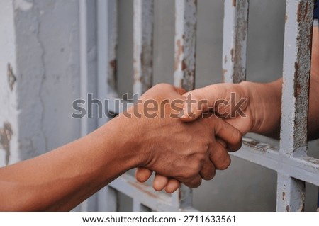 : Close-up of Two Hands Shaking Through Prison Bars Signifying Hope, Farewell, or Reconciliation