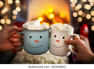 Close-up of two hands with snowman face on cup of hot cocoa with marshmallows. Mom and child relaxing together on a cozy winter evening by fireplace. Enjoy Christmas holidays, happy moments at home. - Powered by Shutterstock