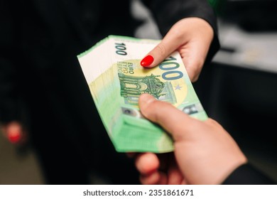 Close-up of two hands of a young woman and a man exchanging 100 euro banknotes to buy and sell. High quality photo