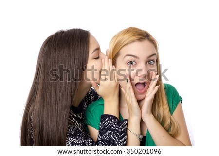Closeup of two happy young girl friends  whispering isolated on white background