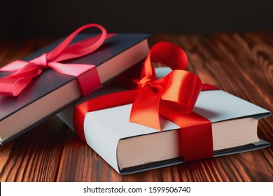 Close-up of two hardback books tied with gift ribbon on a textured wooden background: the concept of good books is a good gift.