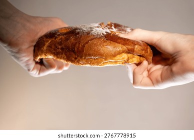 Close-up of two human hands pulling and tearing a loaf of bread from opposite sides. Concept of sharing, friendship, unity, support, and human connection. Symbolic image of cooperation, conflict and compromise, generosity and togetherness. Minimal background, copy space.