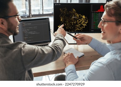 Closeup of two machine learning specialists descanting about new project in office in front of pc, analyzing data. Selective focus on computer screen