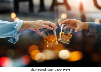 Close-up of two men clink glasses of whiskey drink alcoholic beverage together while at bar counter in the pub after work on colorful background