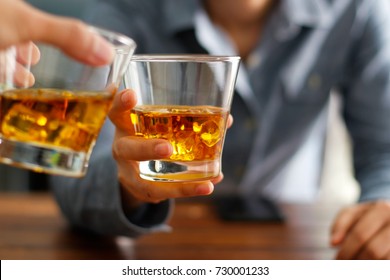Close-up of two men clink glasses of whiskey drink alcoholic beverage together while at bar counter in the pub