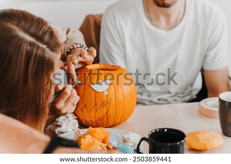 Close-up of two people using a stencil to trace a face design onto a pumpkin in preparation for Halloween carving