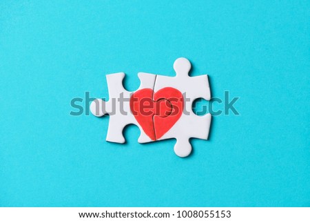 closeup of two pieces of a puzzle forming a heart, depicting the idea that love is a matter of two, on a blue background, with some blank space around it