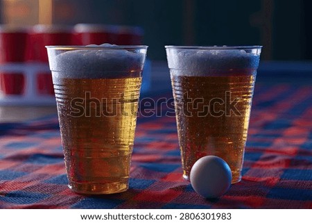 Close-up of two plastic cups of beer with foam, next to a ping pong ball, suggesting a party or game.