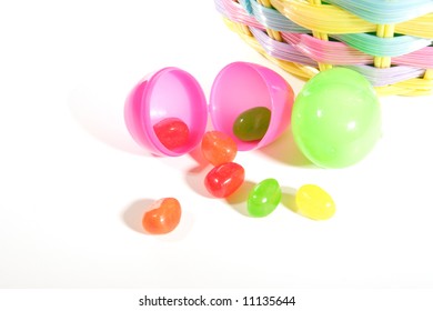 A Closeup Of Two Plastic Easter Eggs On A White Background In Front Of An Easter Basket.  One Egg Has Opened Spilling It's Jelly Beans.