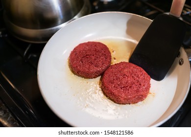 Closeup Of Two Raw Vegan Meat Sausage Patties Cooking On Ceramic Nonstick Frying Pan With Oil Grease Spatula Flipping