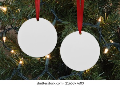 Closeup of two round Christmas Ornaments hanging merrily from a lit up Christmas tree. - Shutterstock ID 2165877603
