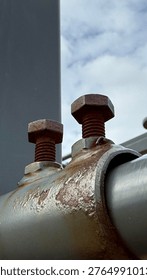 Close-Up of Two Rusty Hex Bolts on Corroded Pipe Clamp Bracket Against Cloudy Sky, Severe Metal Oxidation and Structural Fastener Deterioration, Industrial Infrastructure Maintenance Concept