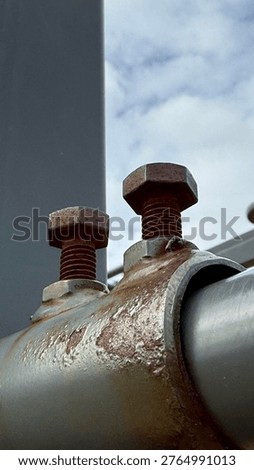 Close-Up of Two Rusty Hex Bolts on Corroded Pipe Clamp Bracket Against Cloudy Sky, Severe Metal Oxidation and Structural Fastener Deterioration, Industrial Infrastructure Maintenance Concept