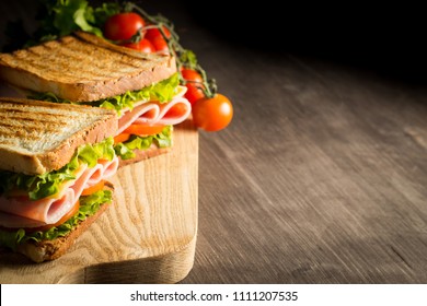 Close-up of two sandwiches with bacon, salami, prosciutto and fresh vegetables on rustic wooden cutting board. Club sandwich concept. - Powered by Shutterstock