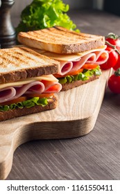 Close-up of two sandwiches with bacon, salami, prosciutto and fresh vegetables on rustic wooden cutting board. Club sandwich concept.