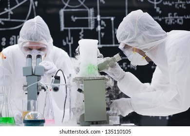 close-up   of two scientists analyzing under microscope in a chemistry lab with a blackboard on the background