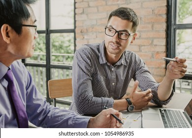 Closeup Of Two Serious Business Men Talking And Working On Project At Loft Office Desk With Brick Wall And Windows In Background