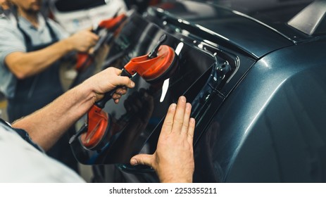 Close-up of two unrecognisable men holding rear window pane to install into back of car. Car maintenance. Garage work. Horizontal indoor shot. High quality photo