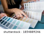 Close-up of two women choosing samples of wall paint. Interior designer consulting a client looking at a color swatch. House renovation concept