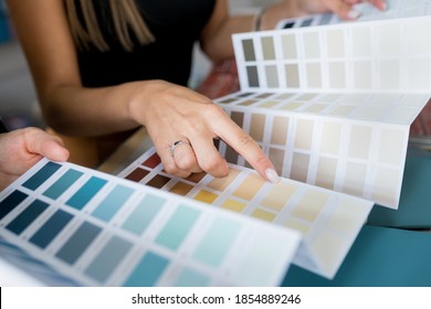 Close-up of two women choosing samples of wall paint. Interior designer consulting a client looking at a color swatch. House renovation concept