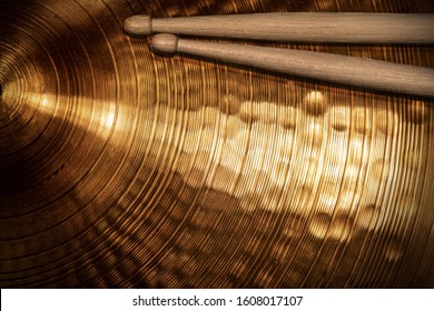 Close-up of two wooden drumsticks on a golden colored cymbal. Percussion instrument