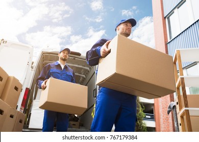 Close-up Of Two Young Delivery Men Carrying Cardboard Box In Front Of Truck
