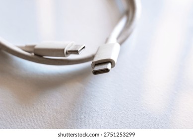 Close-up of a type-C cable with two connectors. The cable is white and flexible, lying on a light surface. Ideal for technology and electronics themes.
