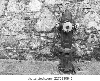 Closeup typical red fire hydrant rusty on the street near stone wall, outdoor. Plumbing for fire hydrant on public footpaths. Fire protection concept. Black and white