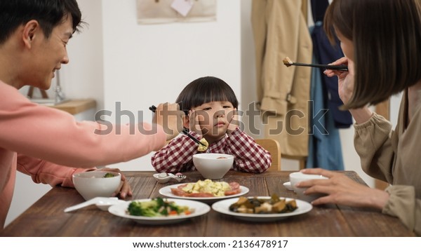 closeup of\
unhappy Asian preschool boy shaking head and saying no to eat at\
dining table to his mom and dad at\
home