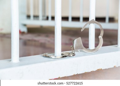 Closeup Of Unlocked Handcuffs Hanging On Jail Bars