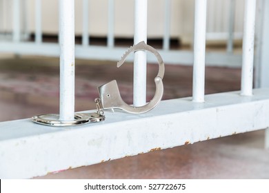 Closeup Of Unlocked Handcuffs Hanging On Jail Bars