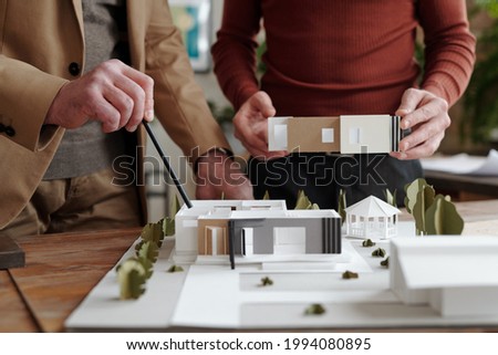 Close-up of unrecognizable architect pointing at house maquette while discussing spaces of future house with colleague [[stock_photo]] © 
