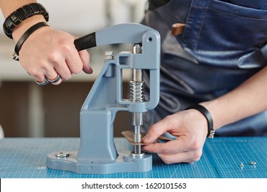 Close-up of unrecognizable artisan in apron using hand press for setting snaps in leather - Powered by Shutterstock