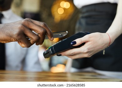 Close-up Of Unrecognizable Black Customer Paying For Bill Through Mobile App In Cafe, Waitress Holding Payment Terminal