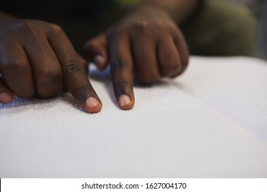 Closeup of unrecognizable blind African man reading braille book while studying in school, copy space