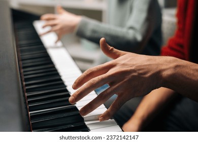 Close-up of unrecognizable child boy playing piano, music teacher sits near and helps with playing during lesson at music school. Kid practicing piano lesson in living room. Concept of music education - Powered by Shutterstock