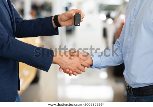 Closeup of\
unrecognizable customer and car dealer shaking hands. Sales\
assistant giving man automatic key from brand new car, having hand\
shake, auto showroom interior,\
cropped