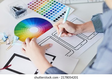 Close-up of unrecognizable designer sitting at desk with papers and drawing interface design for digital devices - Shutterstock ID 2178054201