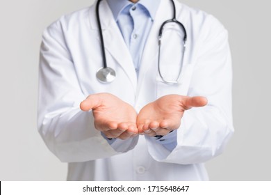 Closeup of unrecognizable doctor holding invisible object on his open palms, standing over white background, cropped image - Powered by Shutterstock
