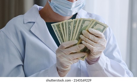 Close-up Unrecognizable Doctor Nurse Medical Worker Surgeon Practitioner In White Coat Protective Face Mask And Latex Gloves Holds Stack Of Money Counts Bills Banknotes Receive Bribe Salary In Clinic