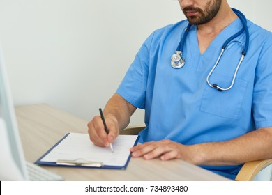 Closeup Of Unrecognizable Doctor  Sitting At Desk In Office Filling In Patient Forms  Against White Background