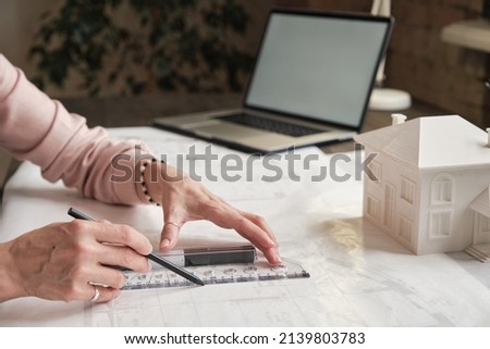 Close-up of unrecognizable female architectural drafter in ring using ruler while working with blueprint of house