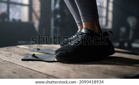 Closeup unrecognizable female athlete legs jumping on wooden box. Fit girl in sneakers using wooden box for fitness training in gym. Athletic woman feet exercising with sports equipment 