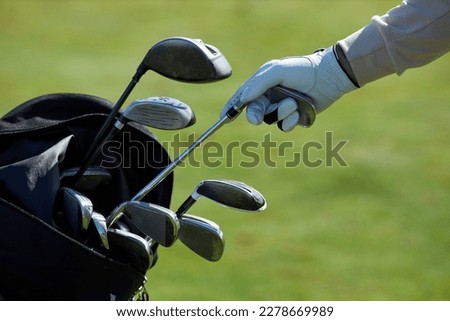 Closeup of unrecognizable golf player choosing club and taking out of golf bag against green grass background
