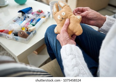 Close-up Of Unrecognizable Granny Sewing Fabric Together While Making Handmade Toy Using Needle At Home