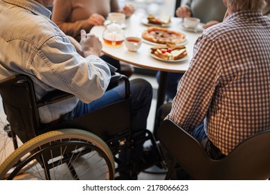 Close-up Of Unrecognizable Handicapped Man In Wheelchair Surrounded By Friends Sitting At Table And Chatting With Friends