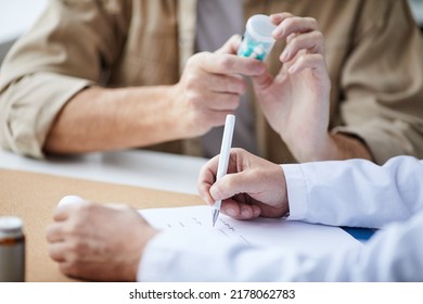 Close-up Of Unrecognizable Male Doctor Sitting At Table And Filling Prescription While Patient Reading Pill Bottle Label