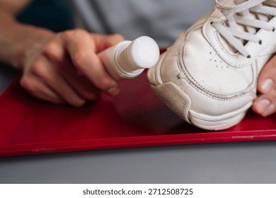 Close-up of unrecognizable man holding using bottle of shoe whitener and painting scuffed surface of dirty white sneaker, illustrating process of cleaning, recoloring, and restoring footwear.