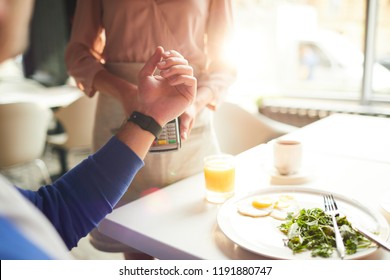 Close-up of unrecognizable man paying for breakfast using smartwatch, he making contactless payment in cafe - Powered by Shutterstock