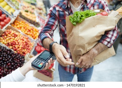 Closeup of unrecognizable man paying via smartwatch while grocery shopping at farmers market, copy space - Powered by Shutterstock